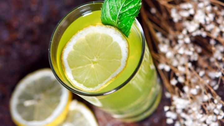 Ein Glas selbstgemachtes Limonadenpulver mit Zitronenscheiben und Minze steht auf einem rustikalen Tisch, umgeben von Trockenblumen.