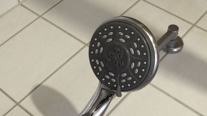 Ein Duschkopf liegt auf einem Fliesenboden, w&auml;hrend er entkalkt wird, um Ablagerungen zu entfernen.