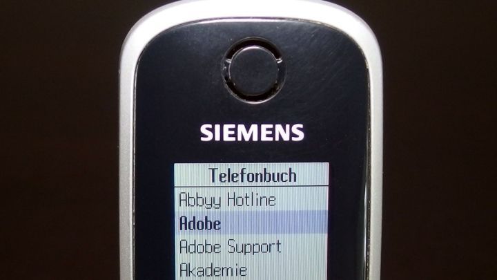 Ein Schnurlostelefon zeigt ein Men&uuml; mit Optionen wie "Telefonbuch" und "R&uuml;ckruf Hotline" in einem dunklen Raum.