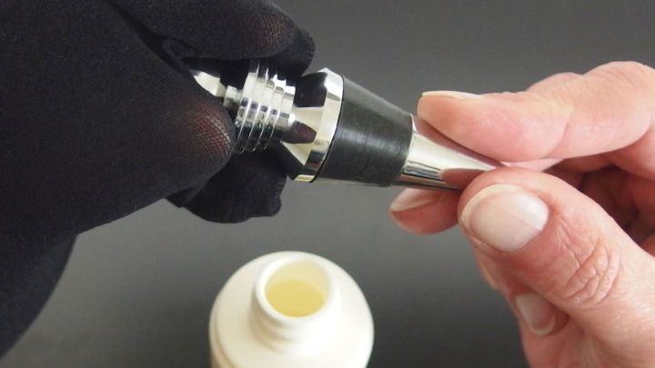 Ein Handschuh h&auml;lt ein Edelstahlteil, das poliert wird; im Hintergrund steht eine Flasche mit einer Polierl&ouml;sung.