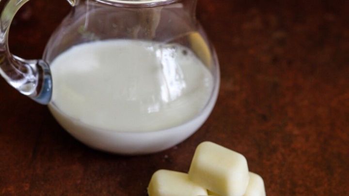 Eine gl&auml;serne Kanne mit Sahne steht neben gefrorenen Sahnew&uuml;rfeln auf einer rustikalen Holzoberfl&auml;che.