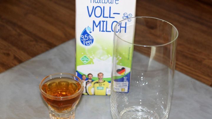 Eine Flasche Vollmilch steht neben einem leeren Glas und einem kleinen Schnapsglas, das einen goldenen Lik&ouml;r enth&auml;lt.