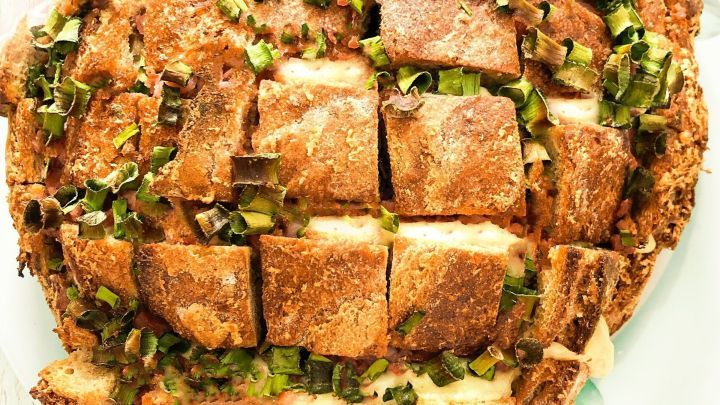 Ein rustikales Pull-away-Brot mit bequemer Aufteilung, garniert mit frischem Schnittlauch auf einem wei&szlig;en Teller.