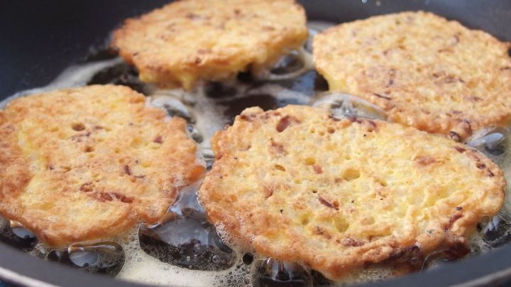 In einer Pfanne braten vier goldbraune Couscous-Bratlinge in sch&auml;umendem &Ouml;l, w&auml;hrend die Umgebung eine k&uuml;chelicher Atmosph&auml;re zeigt.