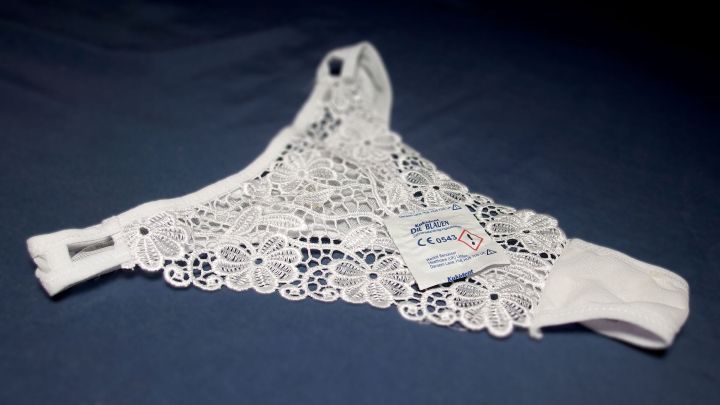 Wei&szlig;e Unterw&auml;sche liegt auf einem dunklen Hintergrund, zeigt filigrane Spitze und ein Etikett. Blutflecken sind nicht sichtbar.