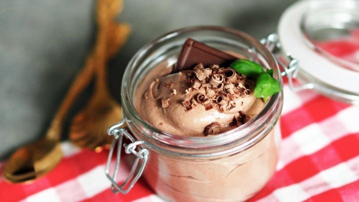 Ein Glas Mouse au Chocolat ist gef&uuml;llt mit cremiger Schokoladenmousse, garniert mit Schokoladenst&uuml;ckchen und frischer Minze, auf einem karierten Tischl&auml;ufer.