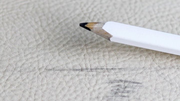 Ein Bleistift liegt auf Kunstleder, w&auml;hrend er eine Markierung hinterl&auml;sst, die entfernt werden soll.