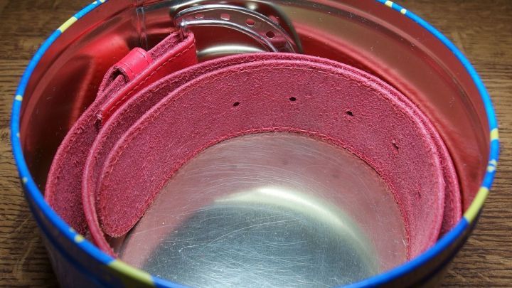 Ein rosa G&uuml;rtel liegt ordentlich in einer runden, bunten Dose, die als Aufbewahrungsort dient.