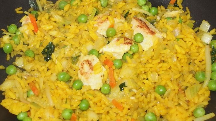 Bunte Reispfanne mit Erbsen, Karotten und St&uuml;ckchen, die in einer Pfanne gl&auml;nzend zubereitet wird.