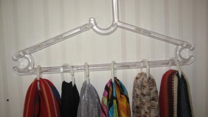 Ein transparenter Kleiderb&uuml;gel h&auml;lt mehrere Schals ordentlich aufgereiht, angeordnet in einem hellen Raum.