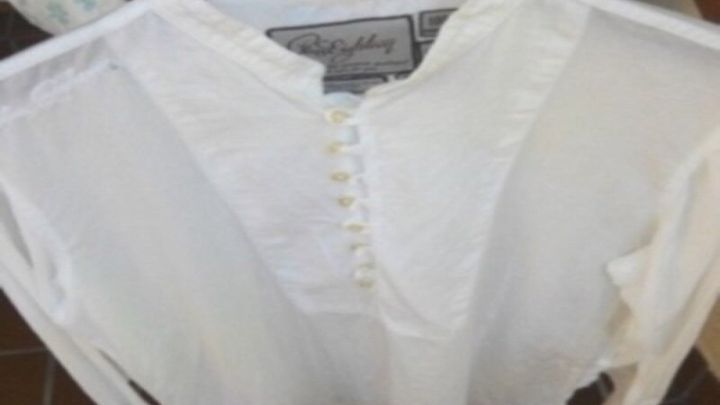 Eine wei&szlig;e Bluse h&auml;ngt auf einem Kleiderb&uuml;gel, bereit zur Behandlung von Rostflecken mit Zitronensaft und Salz.