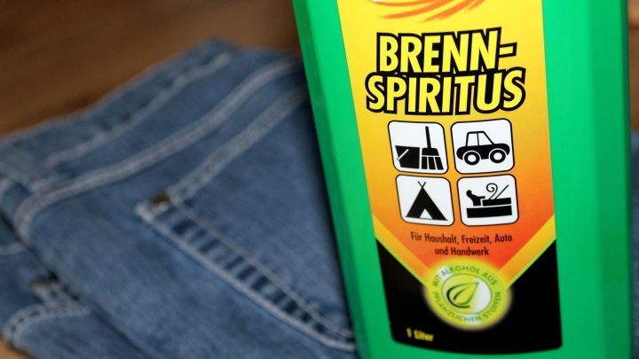 Eine Flasche Brenn-Spiritus steht neben einer Jeans, bereit zum Entfernen von Baumharz aus der Kleidung.