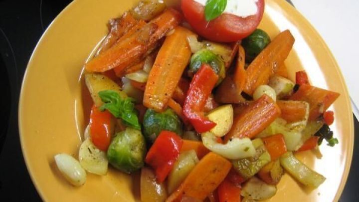 Bunte Gem&uuml;sepfanne mit Paprika, Karotten und Rosenkohl auf Teller; gef&uuml;llte Tomate mit Basilikumbl&auml;ttern oben drauf.