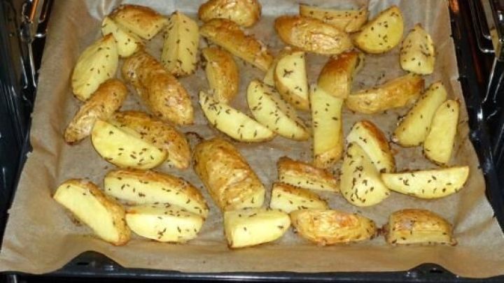 Gebackene K&uuml;mmelkartoffeln liegen auf einem Blech im Ofen, goldbraun und knusprig, umgeben von Backpapier.