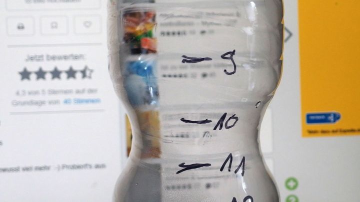 Eine beschriftete Wasserflasche zeigt Markierungen zur Erinnerung, wie viel getrunken werden sollte, vor einem Bildschirm.