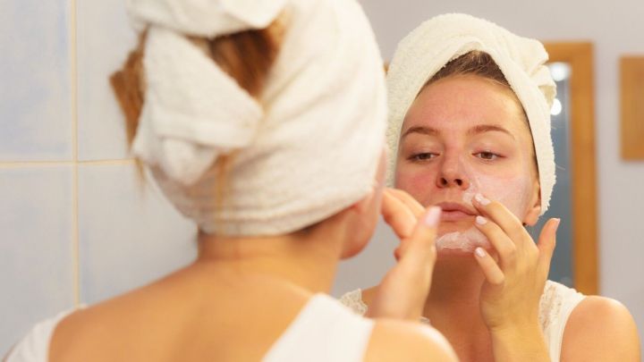 Eine Person tr&auml;gt Aloe vera W&uuml;rfel auf ihr Gesicht auf, w&auml;hrend sie sich im Badezimmer vor einem Spiegel betrachtet.