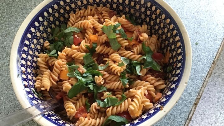 Ein bunter Nudelsalat wird in einer stilvollen Sch&uuml;ssel serviert, angereichert mit frischem Gem&uuml;se und Kr&auml;utern.