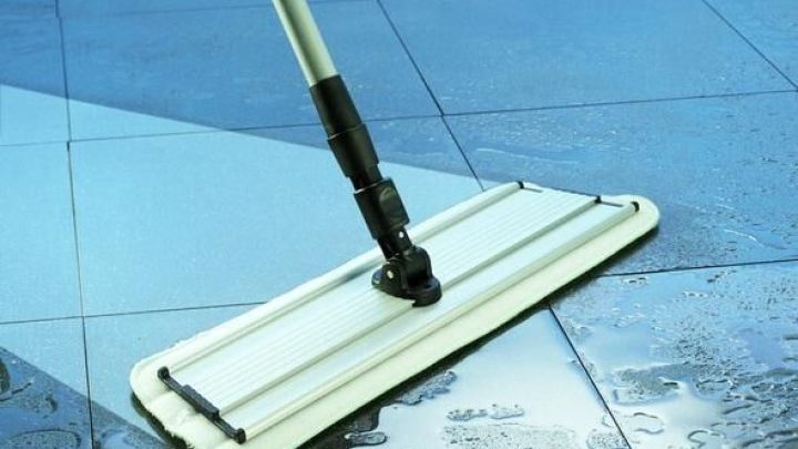 Ein Wischmopp reinigt schnell den nassen Boden in einem modernen, lichtdurchfluteten Raum mit glatten Fliesen.