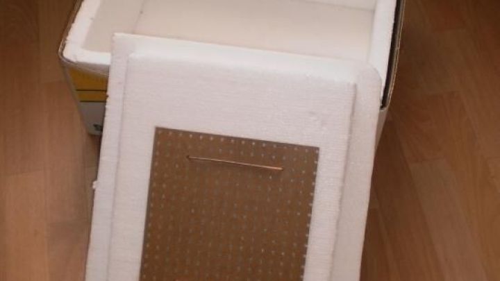 Eine K&uuml;hlbox steht offen auf einem Holzboden, w&auml;hrend der Deckel daneben liegt. Der Kontext zeigt einen Raum mit Vorh&auml;ngen.