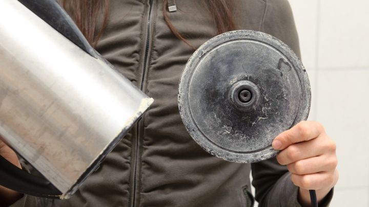 Ein Wasserkocher mit Ablagerungen wird von einer Person gehalten, um effektiv mit Zitronens&auml;ure entkalkt zu werden.