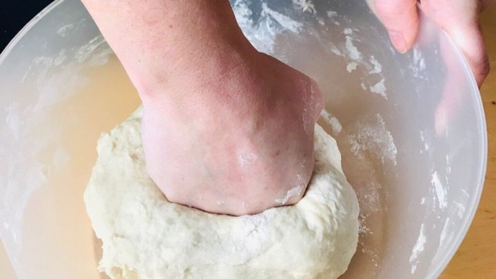 Eine Hand knetet Teig in einer gro&szlig;en Sch&uuml;ssel, um einen glatten, homogenen Teig in einer hellen K&uuml;chenumgebung zu schaffen.