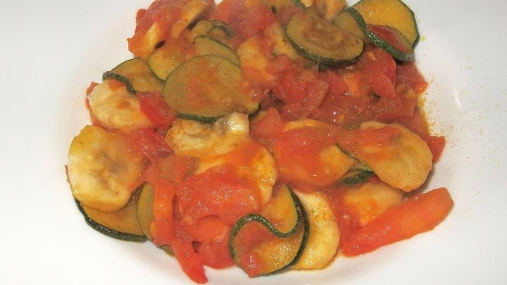 Die Zucchini-Pfanne zeigt eine bunte Mischung aus gebratenen Zucchini, Banane und Tomaten auf einem wei&szlig;en Teller.