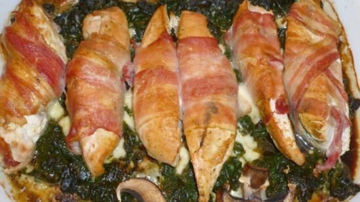 Saftige H&uuml;hnerbrustfilets im Speckwickel liegen auf einem Bett aus Pilzen, Spinat und geschmolzenem Mozzarella.