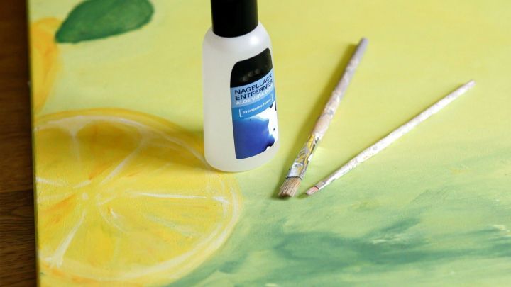 Eine Flasche Nagellackentferner steht neben zwei pinselbetriebenen Farbwerkzeugen auf einer gemalten, gelben Leinwand.