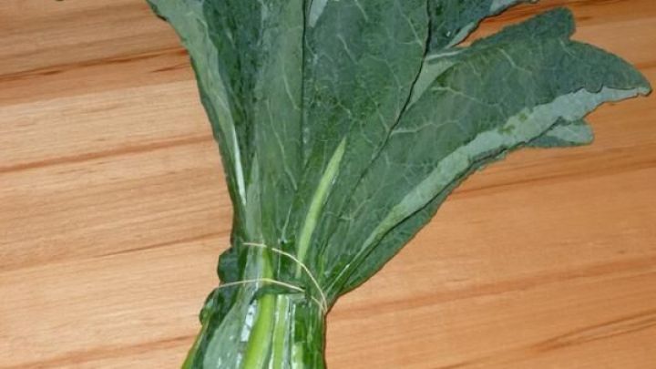 Ein B&uuml;ndel frischer Schwarzkohl liegt auf einer Holzoberfl&auml;che, bereit zur Zubereitung f&uuml;r knusprige Chips.