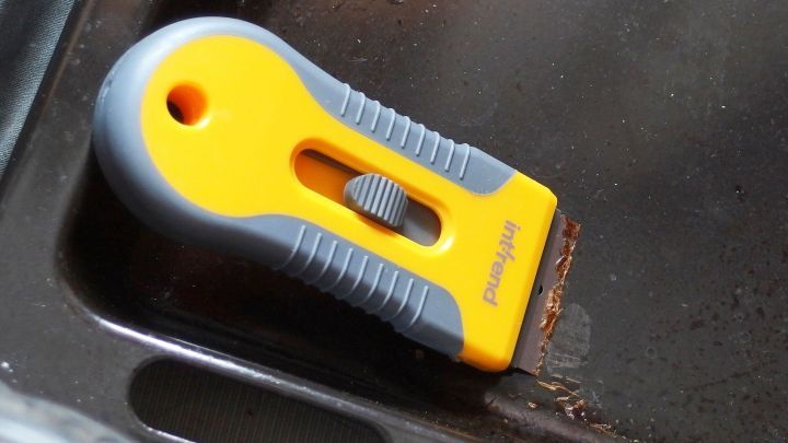 Ein gelber Schaber liegt auf einem Backblech aus Emaille, w&auml;hrend Schmutz entfernt wird, um die Reinigung zu erleichtern.