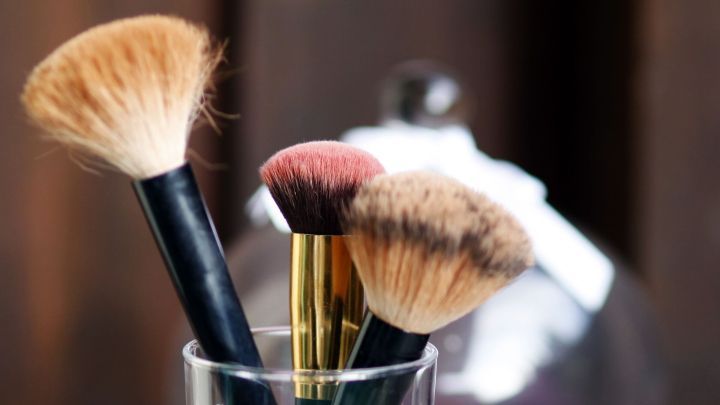 Ein eleganter Glasbeh&auml;lter mit Pinselhaltern zeigt Makeup-Pinsel, die in dekorativem Sand stehen, auf einem Holztisch.