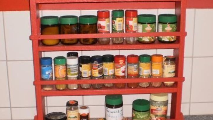 Ein rotes Gew&uuml;rzregal steht auf einem grauen Boden und zeigt verschiedene Gew&uuml;rze in Gl&auml;sern und Dosen.