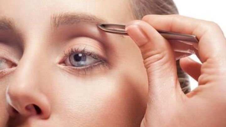 Eine Pinzette zupft eine Augenbraue, w&auml;hrend eine Person die Augen schlie&szlig;t. Der Fokus liegt auf dem Augenbereich.