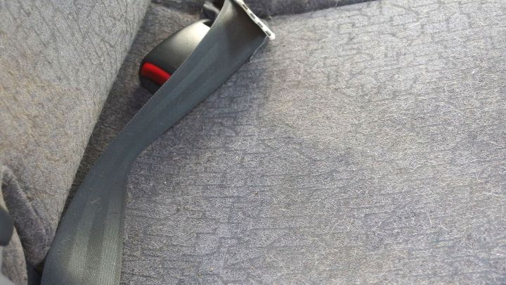 Ein grauer Autositz zeigt einen Sicherheitsgurt, w&auml;hrend der Sitz leicht verschmutzt ist, was Reinigung erfordert.