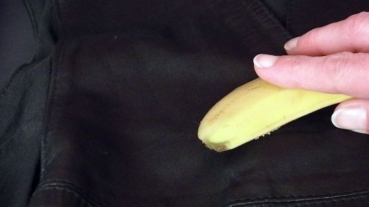 Eine Hand reibt eine Bananenschale &uuml;ber eine dunkle Lederoberfl&auml;che zur Pflege, im Hintergrund ist eine weitere Ledertextur sichtbar.