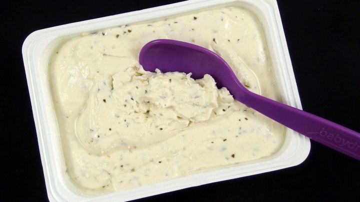 Eine Schale Frischk&auml;se mit einer lila L&ouml;ffel liegt auf einem schwarzen Untergrund und zeigt eine cremige Textur.