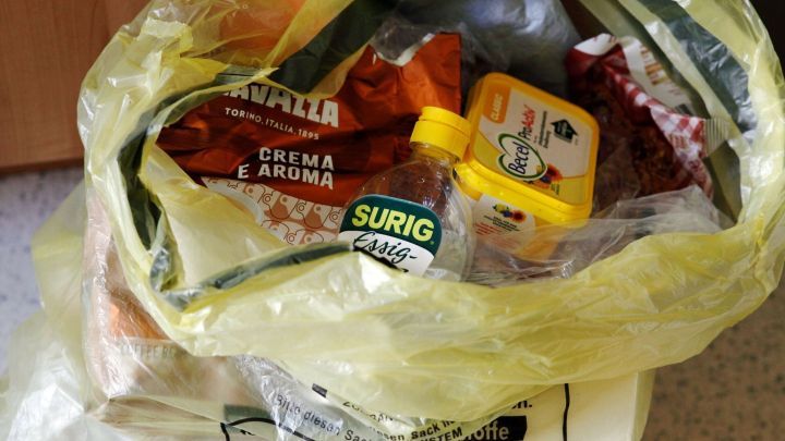 Ein gelber Einkaufsbeutel ist voll mit Lebensmitteln und Utensilien, ideal zum leichteren Erstellen einer Einkaufsliste.