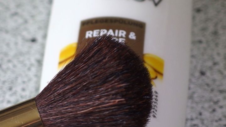Ein Pinsel liegt vor einem Produkt mit der Aufschrift "REPAIR & CARE", das zur Pflege harter Pinsel dient.