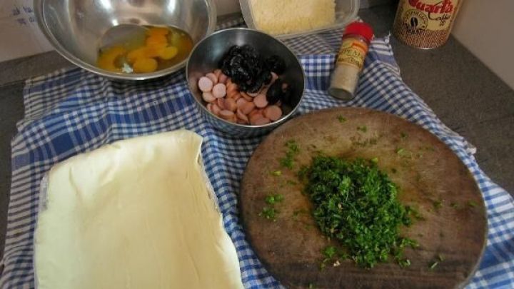 Auf einem K&uuml;chentisch sind Zutaten f&uuml;r einen Ei-Auflauf im Schlafrock vorbereitet: Eier, Schinken, K&auml;se und frische Kr&auml;uter.