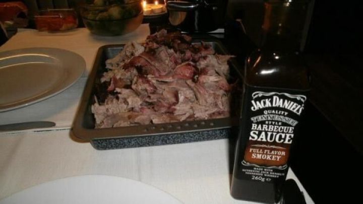 Pulled pork liegt in einer Auflaufform auf einem gedeckten Tisch, daneben steht eine Flasche Jack Daniel's Barbecue Sauce.