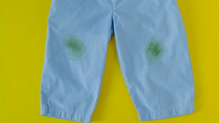 Blaues Kinderhosenpaar liegt auf einem gelben Hintergrund, mit gr&uuml;nen Grasflecken auf den Knien.