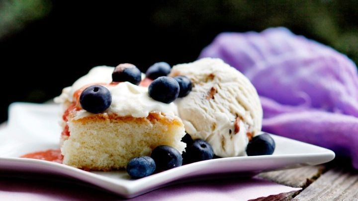 Ein leckerer Wasser/&Ouml;l Kuchen mit Beeren und Eis auf einem wei&szlig;en Teller, serviert in einer nat&uuml;rlichen Umgebung.