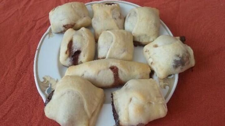 Auf einem Teller liegen mehrere kleine Schoko-Bananen-Taschen, die frisch gebacken auf einem roten Tisch serviert werden.