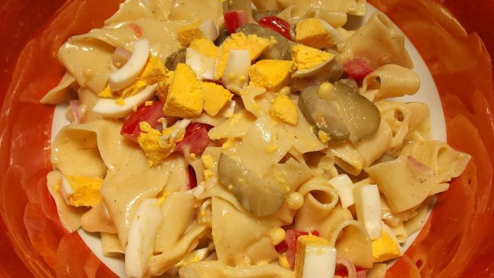 Ein bunter Nudelsalat liegt in einer Sch&uuml;ssel, gemischt mit Gem&uuml;se und Eiern, bereit zum Servieren bei einer Feier.