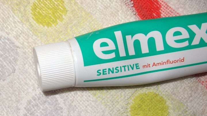 Eine Zahnpasta-Tube liegt auf einem wei&szlig;en Tuch mit bunten Punkten, bereit zum Entfernen von Grasflecken.