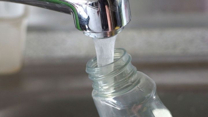 Eine Wasserleitung f&uuml;llt eine Glasflasche, um Glasreiniger zu verd&uuml;nnen. Im Hintergrund ist eine Arbeitsfl&auml;che sichtbar.