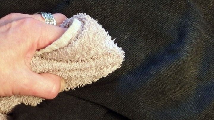 Eine Hand hält ein Tuch, das auf schwarzem Stoff reibt, um Waschmittelrückstände zu entfernen.