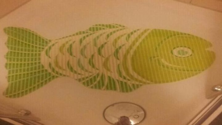 Eine gr&uuml;ne Badematte zeigt ein Fischdesign und liegt auf einem hellen Boden umgeben von Badezimmerfliesen.