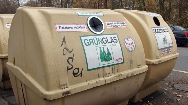 Altglascontainer stehen am Stra&szlig;enrand; ein Container tr&auml;gt das Schild "GR&Uuml;NGLAS" mit Abbildungen von Flaschen.