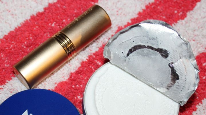 Ein Lippenbalsam und eine Tube Creme stehen auf einem gestreiften Tuch, bereit f&uuml;r schnelle Lippenpflege gegen spr&ouml;de Lippen.